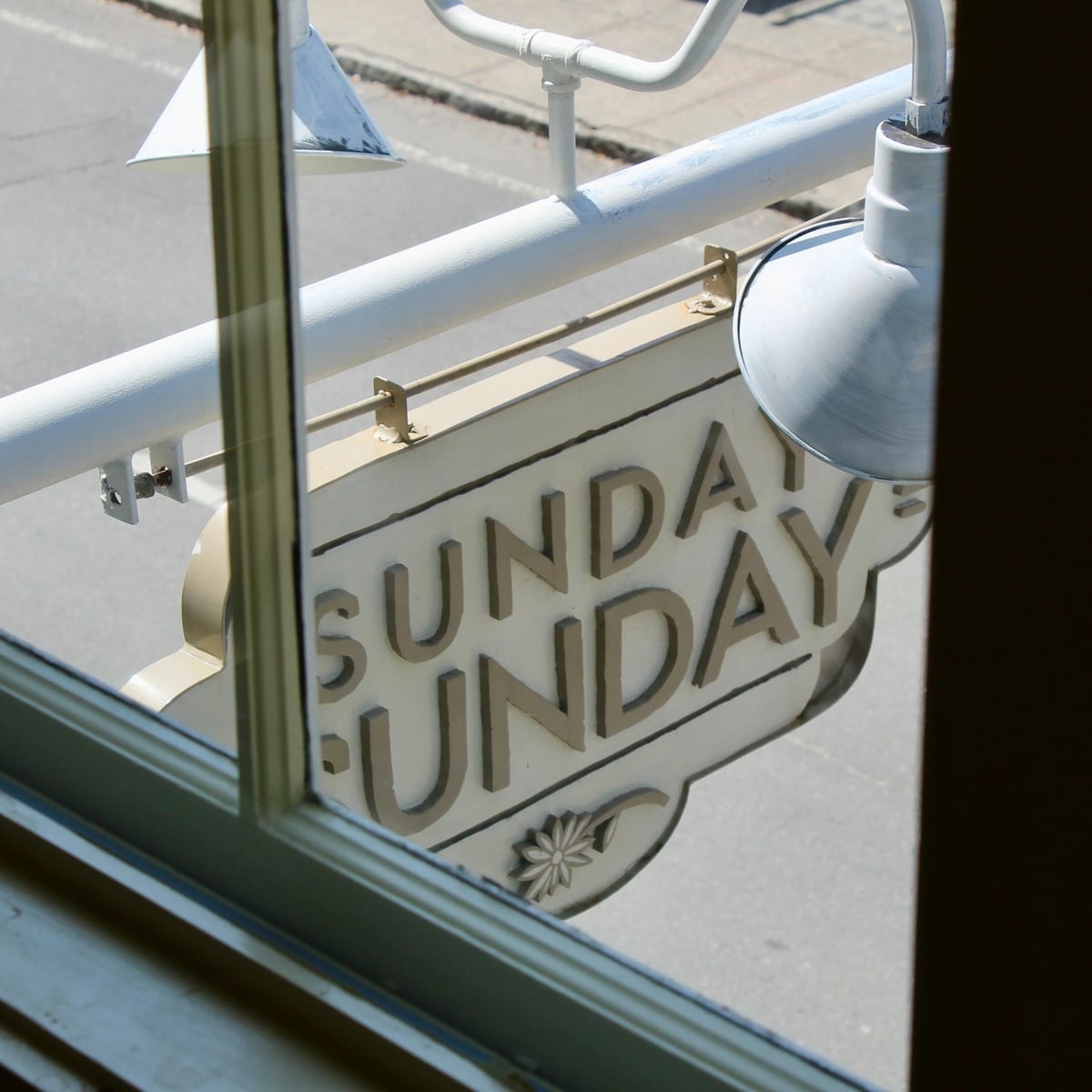 The Sunday Sunday blade sign hanging on West State Street, seen through a window